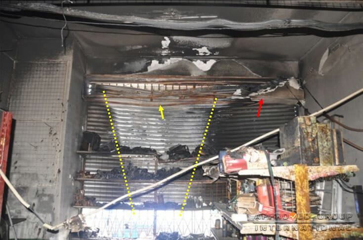 Photograph 2: A distinct V-pattern (yellow dotted lines) was seen at the rear roller shutter of SL1 which indicates that the fire was intense at the lower section. Note the roller shutter casing at the end was partially charred (red arrow) while the metal frame located at the middle section was severely oxidized (yellow arrow).