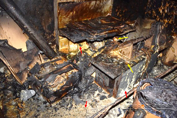 Photograph 3: One of the areas with severe fire damage showing residues of solidified polyurethane foam (red arrows) from the ruptured polyurethane foam spray cans (yellow arrow).